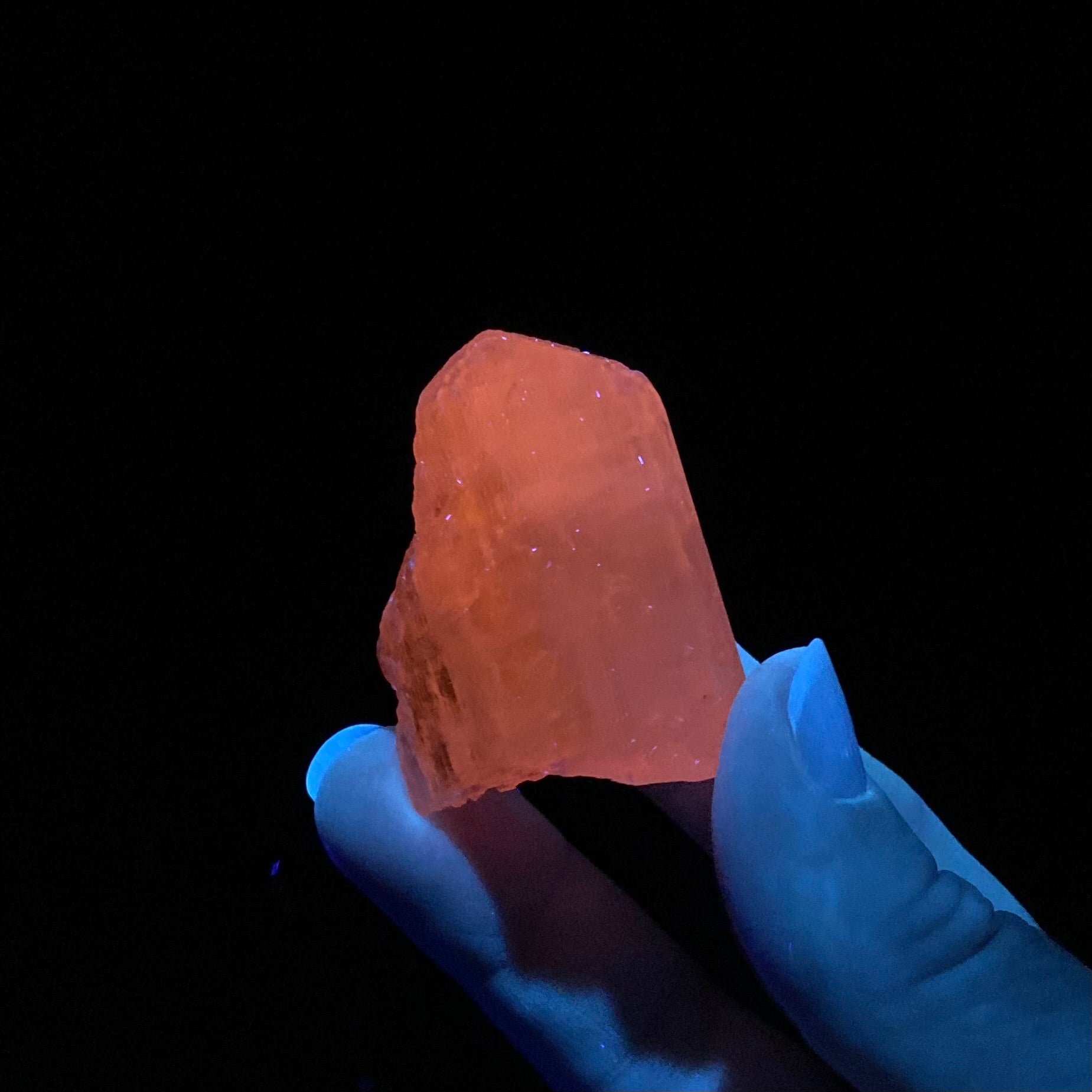 Orange crystal held by a hand against a black background